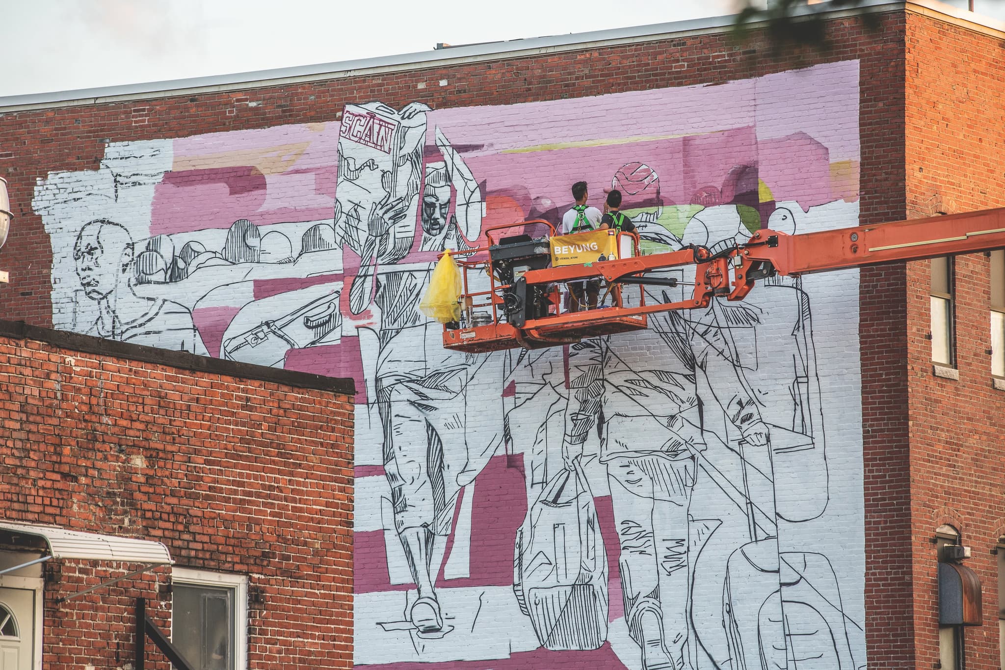 An artist paints a mural from the perch of a forklift.