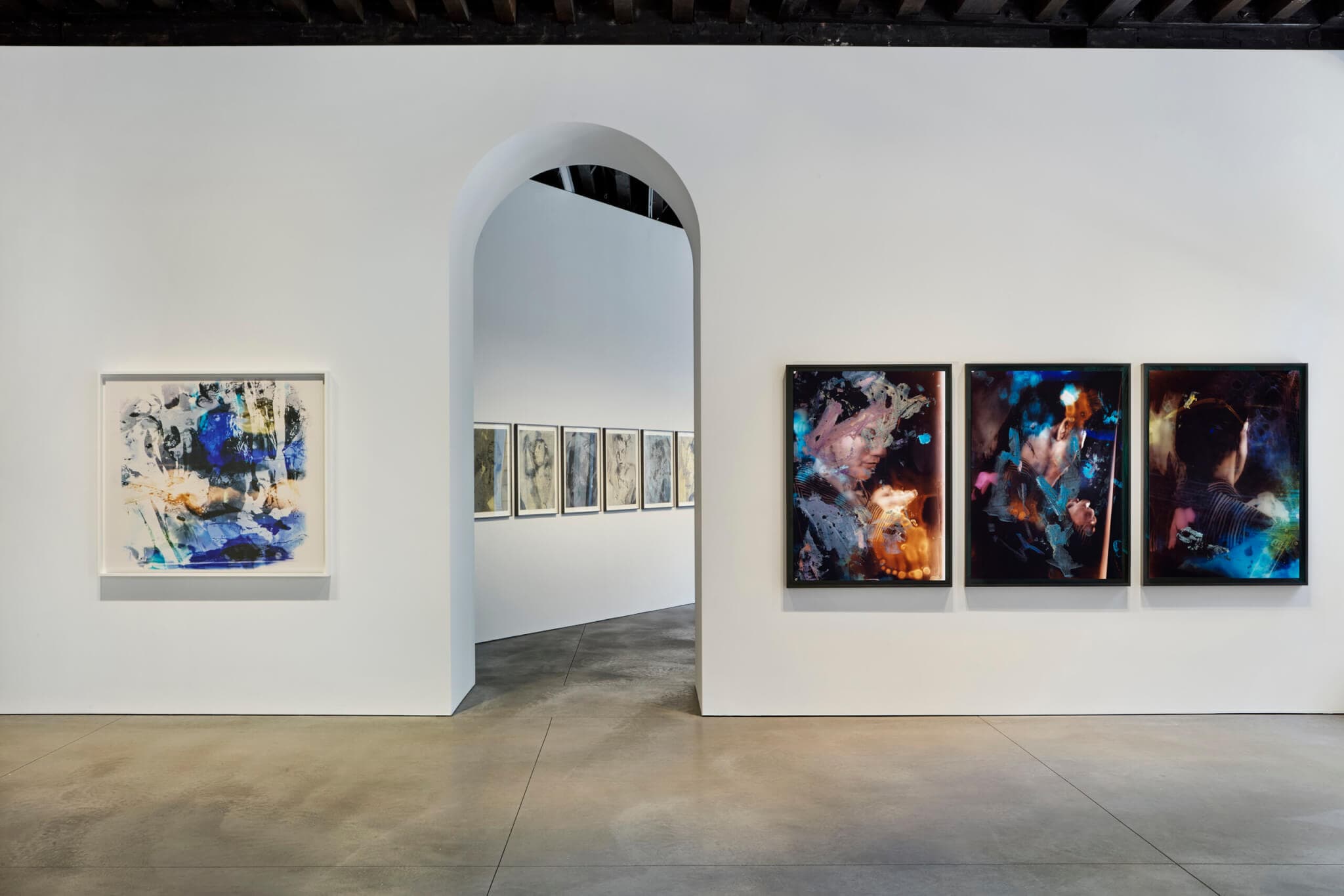 A triptych hangs to the right of a curved doorway in a gallery.